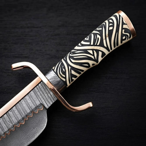 Close-up view of a 12-inch Musso-style Bowie knife showing a carved black-and-white patterned handle, copper double crossguard, and copper Damascus steel blade detailing on a black wood background.