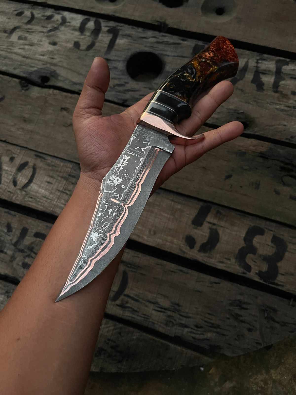 Hand-forged Copper Damascus Bowie knife showcased on natural wood, featuring unique blade patterns.