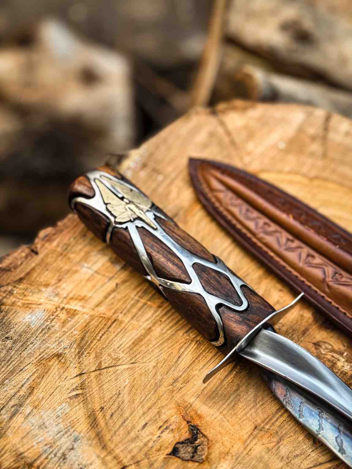 Close-up macro view of a handcrafted Subtle Knife replica handle showing intricate silver metalwork and gold inlay details on dark wood, resting on a rustic log for USA fantasy collectors.