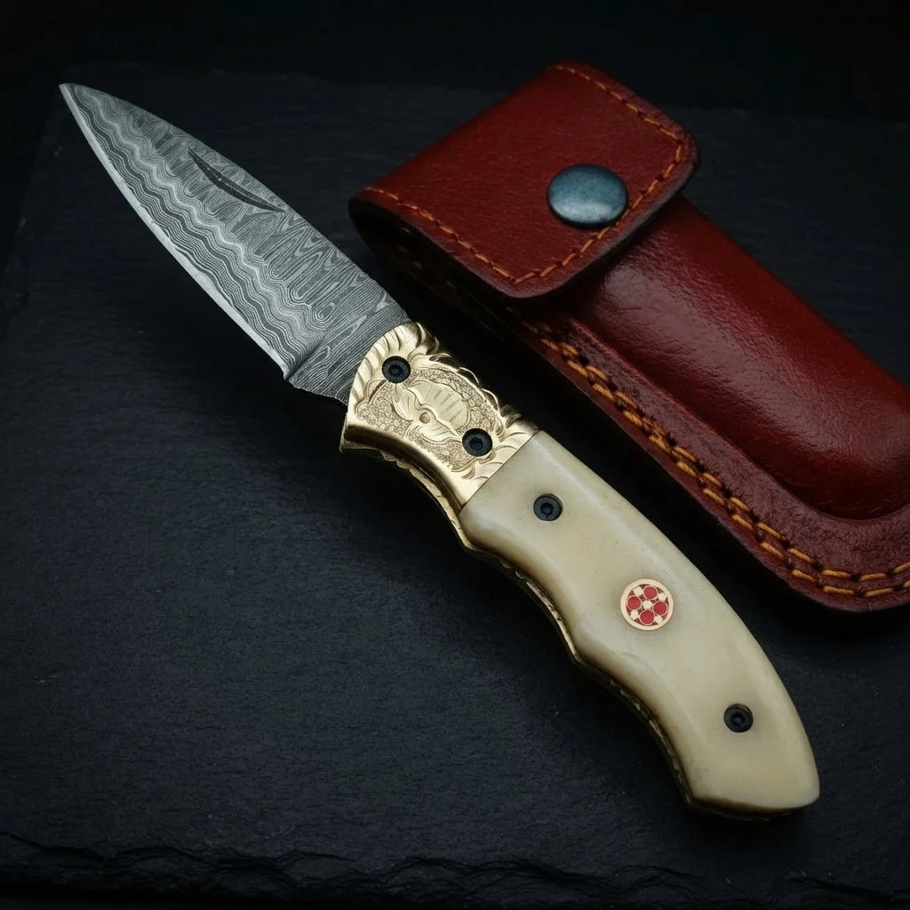 Damascus drop point folding knife — hand-engraved brass bolster and mosaic pin close-up