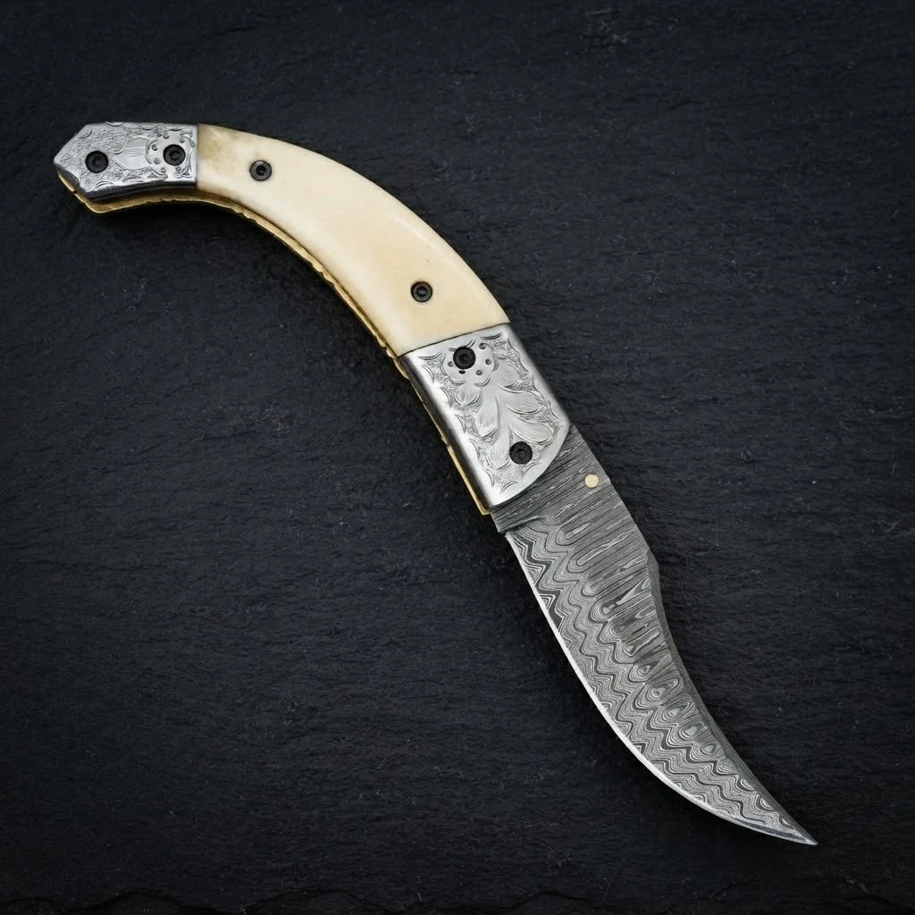 Damascus folding knife — hand-engraved steel bolster close-up