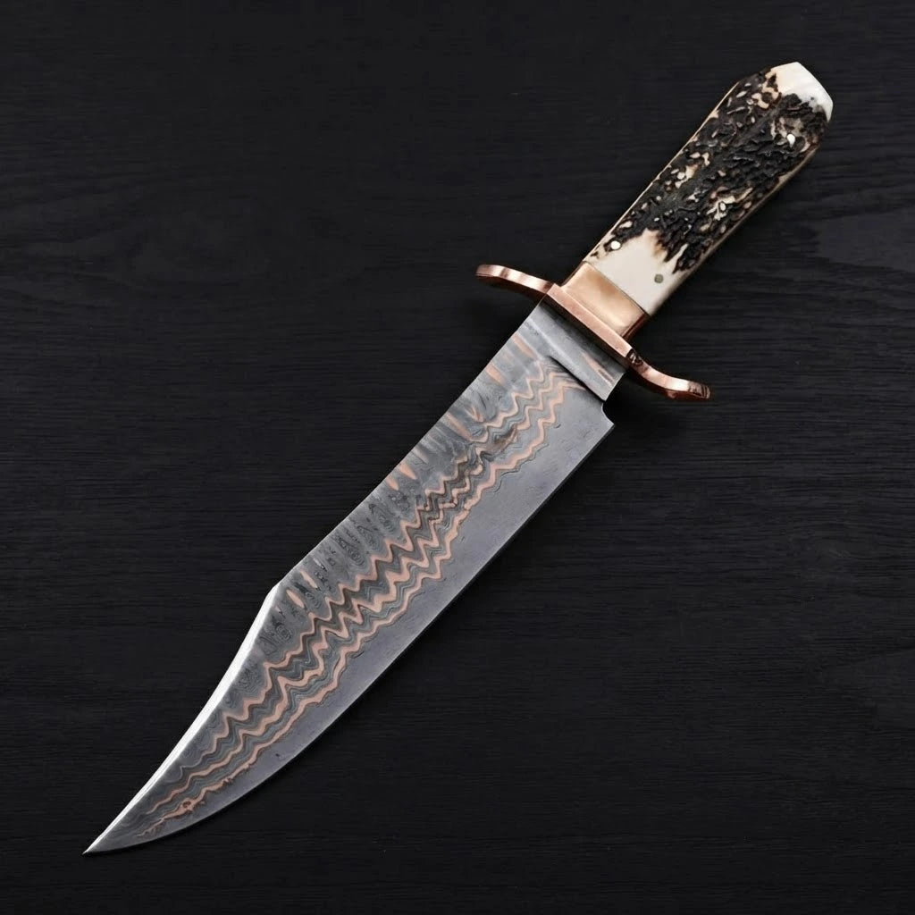 A diagonal top-down view of a 12-inch Copper Damascus Bowie knife featuring a copper double guard and a textured stag antler handle on a dark wood background