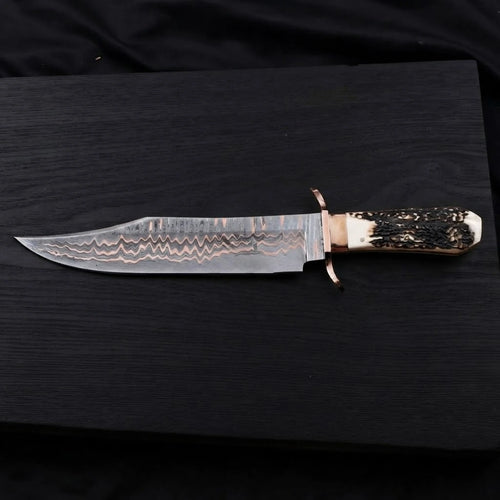Horizontal view of a 12-inch Copper Damascus Bowie knife with a copper double guard and a textured stag antler handle on a dark wood background