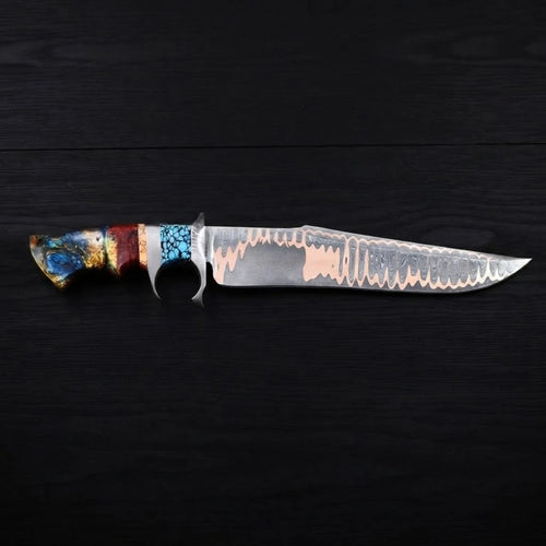 Horizontal profile view of a Copper Damascus Bowie knife with a steel double guard, turquoise stone accent, and multi-colored resin handle on a dark wood background.
