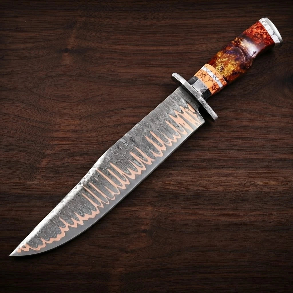 A full diagonal profile view of a custom Copper Damascus steel Bowie knife, showcasing its distinctive layered wavy blade pattern with copper tones, a steel handguard, and a vibrant orange-red fire resin and faux stag hybrid handle, resting on a dark walnut wood grain background