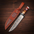A handcrafted Copper Damascus steel Bowie knife featuring a long clip-point blade with visible copper layers, a dark metal handguard, and a hybrid fire-resin and faux stag horn handle, displayed next to its custom brown leather sheath with alligator-skin texture inserts on a dark wood background.