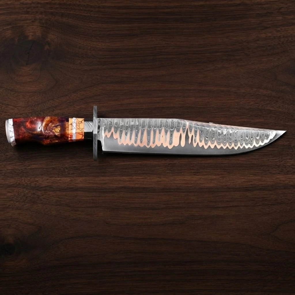 A side profile view of a custom Copper Damascus Bowie knife laying perfectly horizontal on a dark walnut wood background, highlighting the distinct copper-layered pattern on the blade, a steel handguard, and a segmented fire resin handle with orange and white spacers.