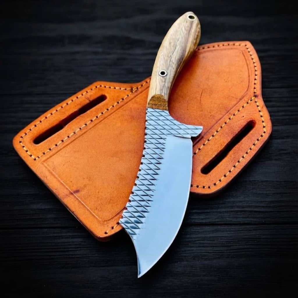 Cowboy Cutter Knife featuring a cross-hatched rasp steel blade and natural wood handle resting on top of a tan leather pancake sheath on a dark wood background.