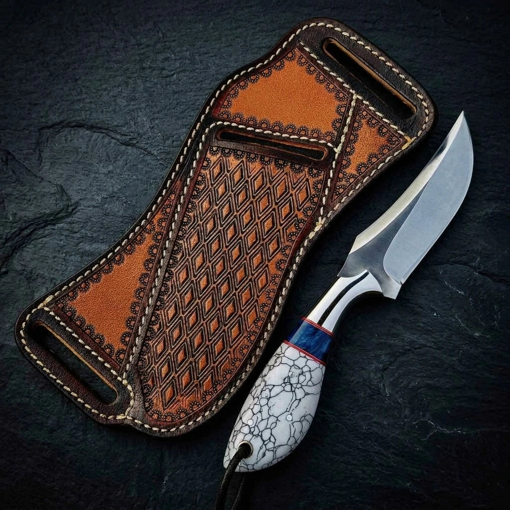 A custom fixed-blade hunting knife with a polished steel blade and a white cracked-pattern handle with blue accents, displayed next to an intricately carved and stitched brown leather sheath on a dark slate background
