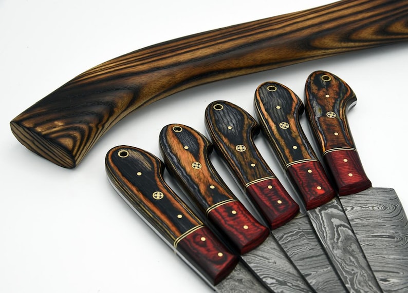 Close-up view of two-tone resin wood knife handles with brass mosaic pins and lanyard holes on a 5-piece Damascus steel kitchen knife set over a white background.