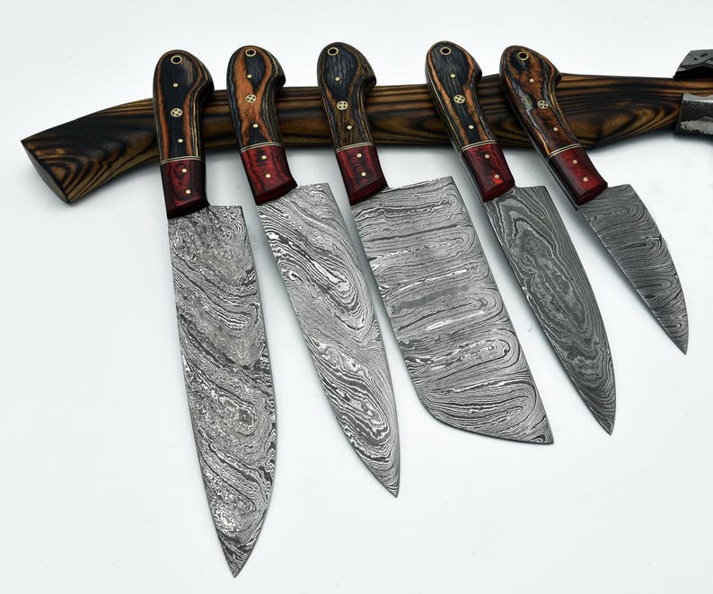 5-piece Damascus steel kitchen knife set with two-tone resin wood handles and mosaic pins, lined up on a white background with a wooden accent.