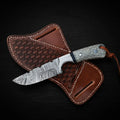 Damascus steel Buckaroo ranch knife with a honeycomb pattern resin handle and leather lanyard, resting on a brown basket-weave leather pancake sheath over dark wood.