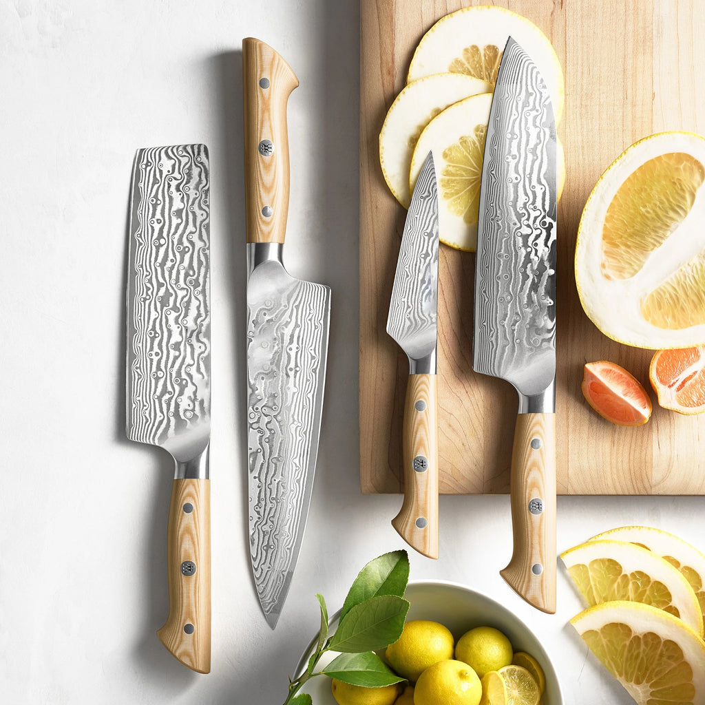 Handmade Damascus steel kitchen knives featuring light wood handles with mosaic pins, displayed flat lay next to a wooden cutting board with sliced citrus fruits.