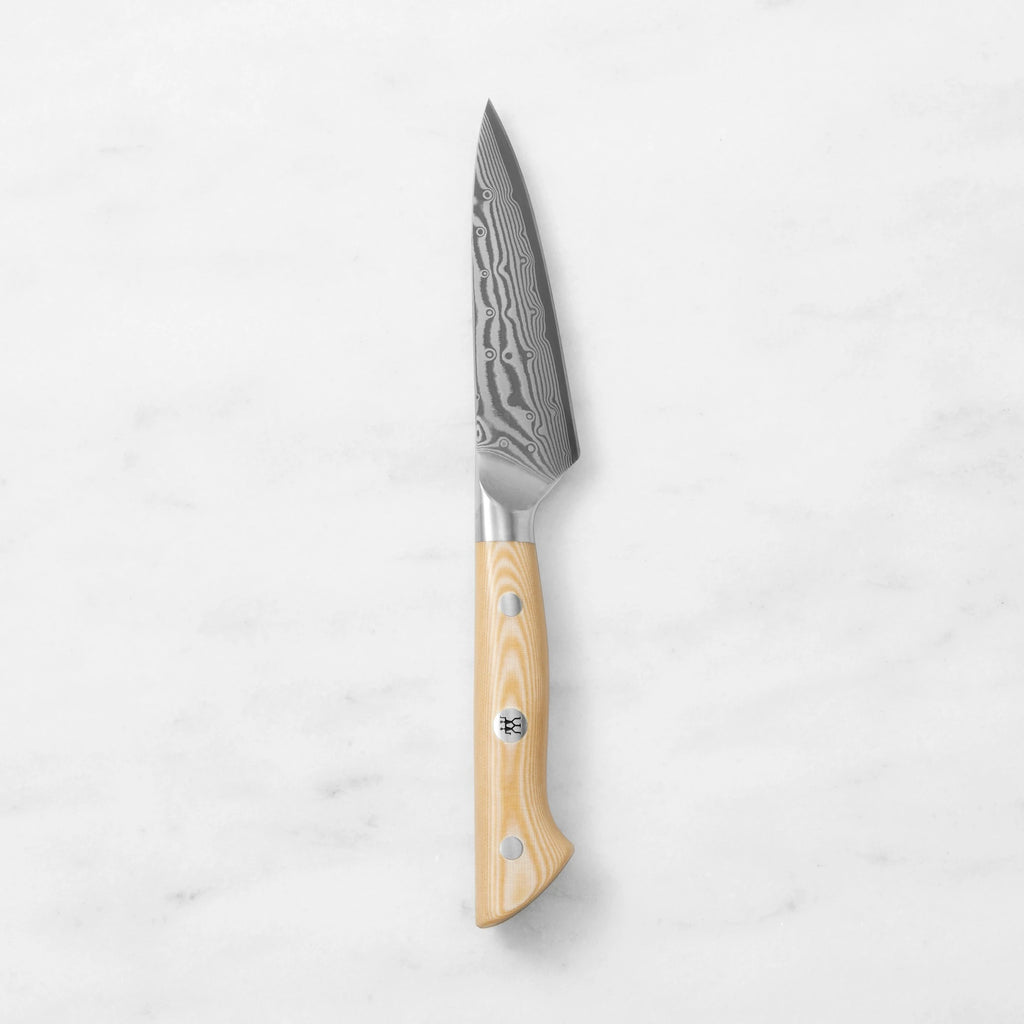 Damascus steel paring knife with a natural light wood handle and mosaic pin, centered vertically against a smooth white marble background