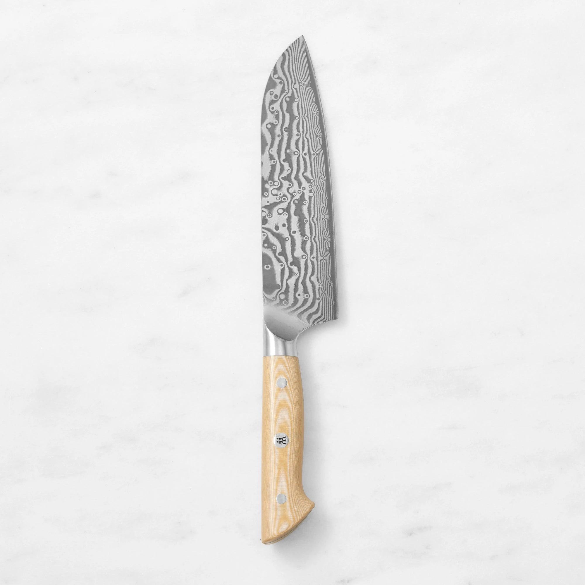 Damascus steel Santoku knife with a light wood handle and mosaic pin, centered vertically against a smooth white marble background.