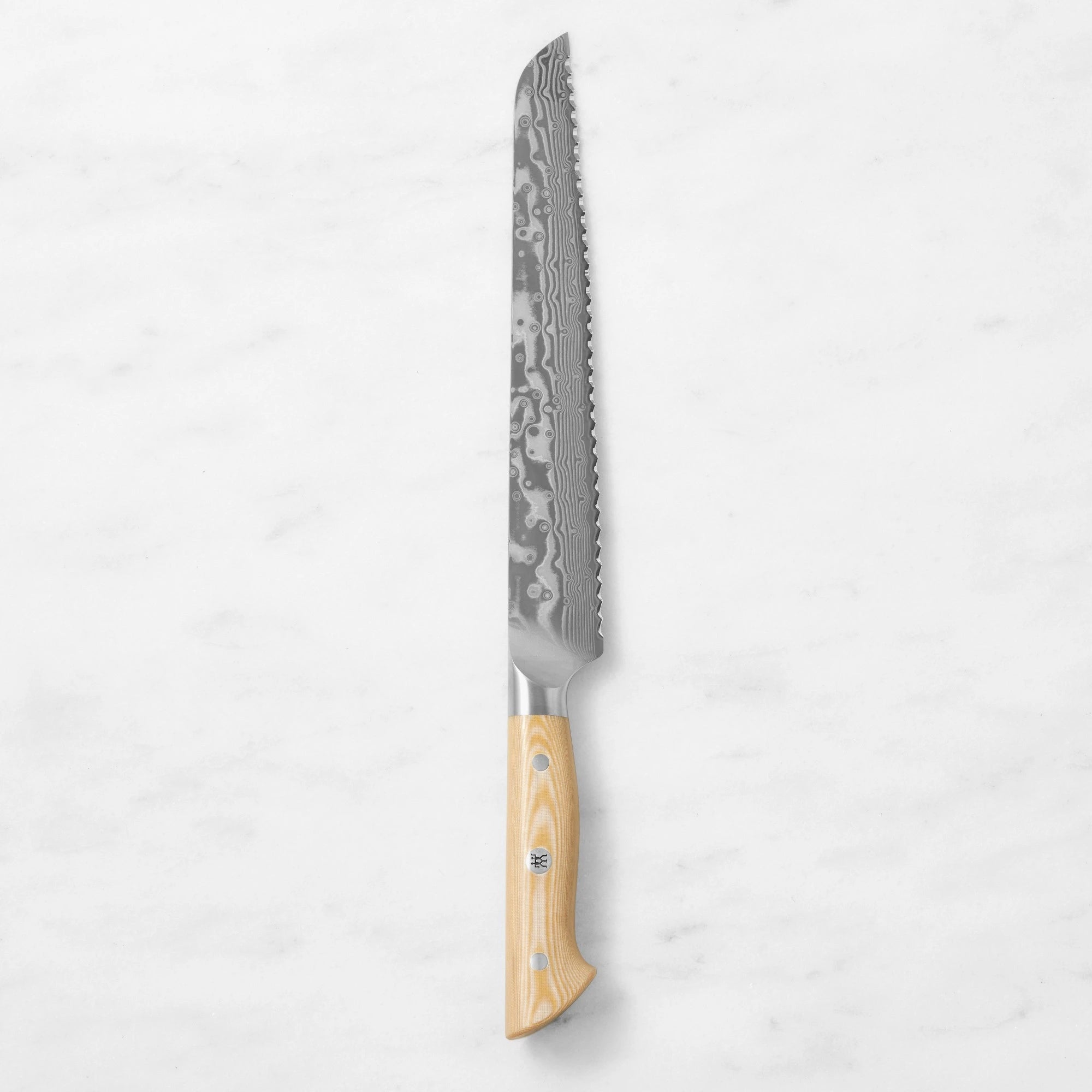 Damascus steel serrated bread knife with a natural light wood handle, centered vertically against a smooth white marble background