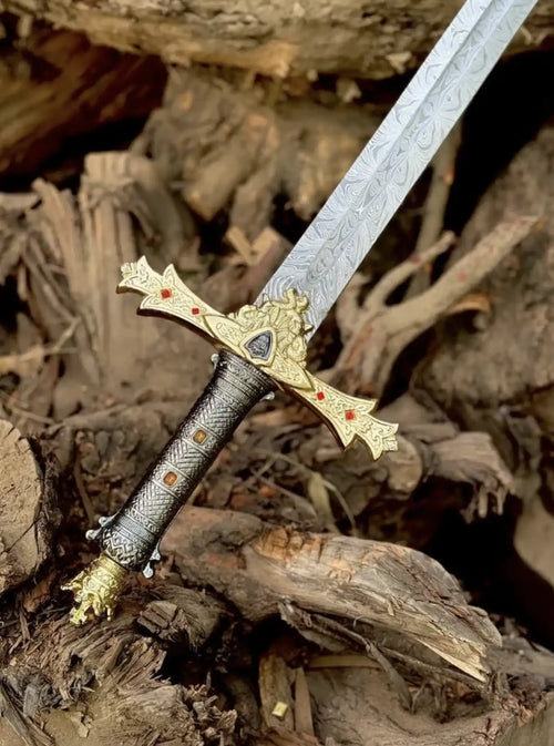 Extreme close-up shot of a custom Damascus steel sword hilt, showcasing an intricately carved black textured handle, a golden crossguard with red gemstone accents, and the detailed wavy pattern of the steel blade.