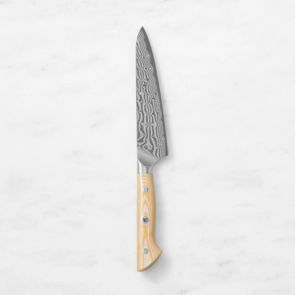 Damascus steel utility prep knife with a natural light wood handle and mosaic pin, centered vertically against a smooth white marble background.