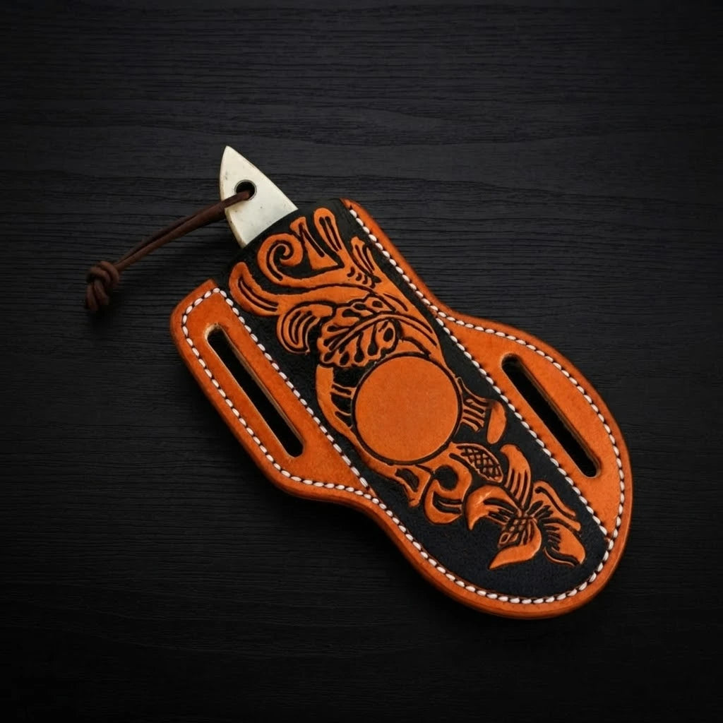 Handmade gut hook cowboy knife sheathed in a hand-tooled floral leather pancake sheath, showing only the white camel bone handle tip on a black wood surface