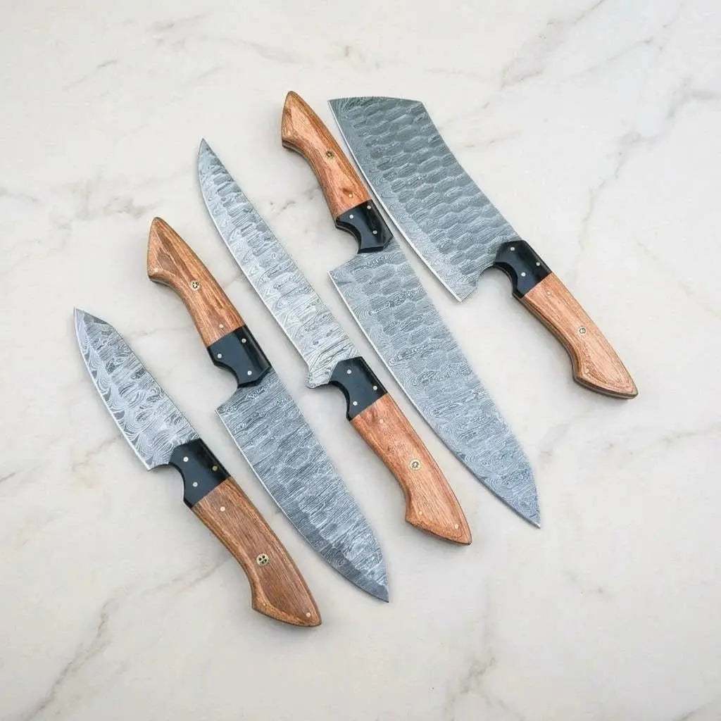 Hammered Damascus steel kitchen knives with Pakka wood handles and black G10 bolsters on marble