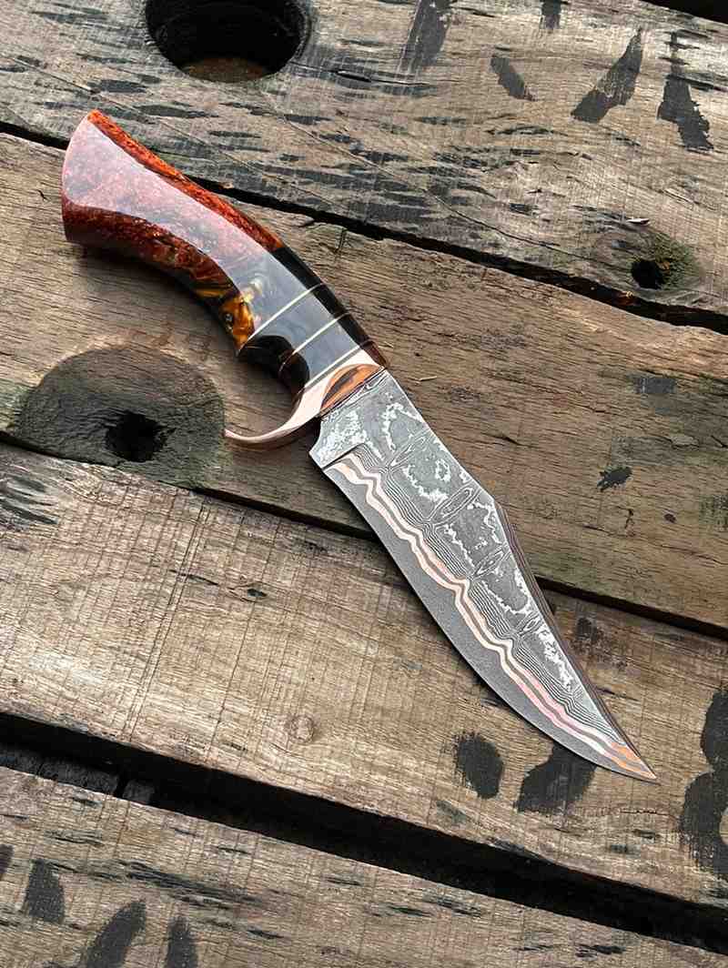 Hand-forged Copper Damascus Bowie knife featuring an intricate custom resin handle, displayed on rustic wood