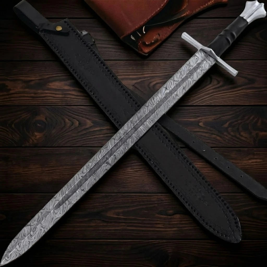 A hand-forged medieval short sword featuring a patterned Damascus steel blade with a full-length fuller, a silver crossguard, a ribbed black handle, and a fluted pommel, displayed crossed over its black leather scabbard on a dark wood background.