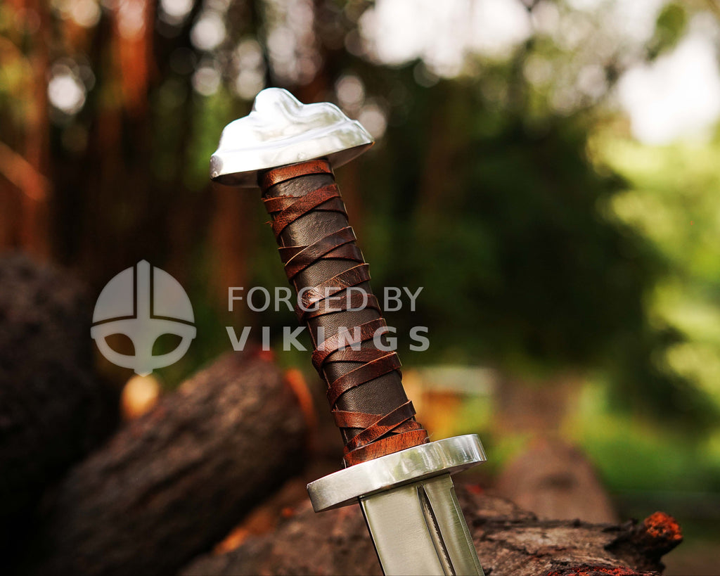 Hand-forged Viking Seax knife with detailed blade engravings resting on wooden logs