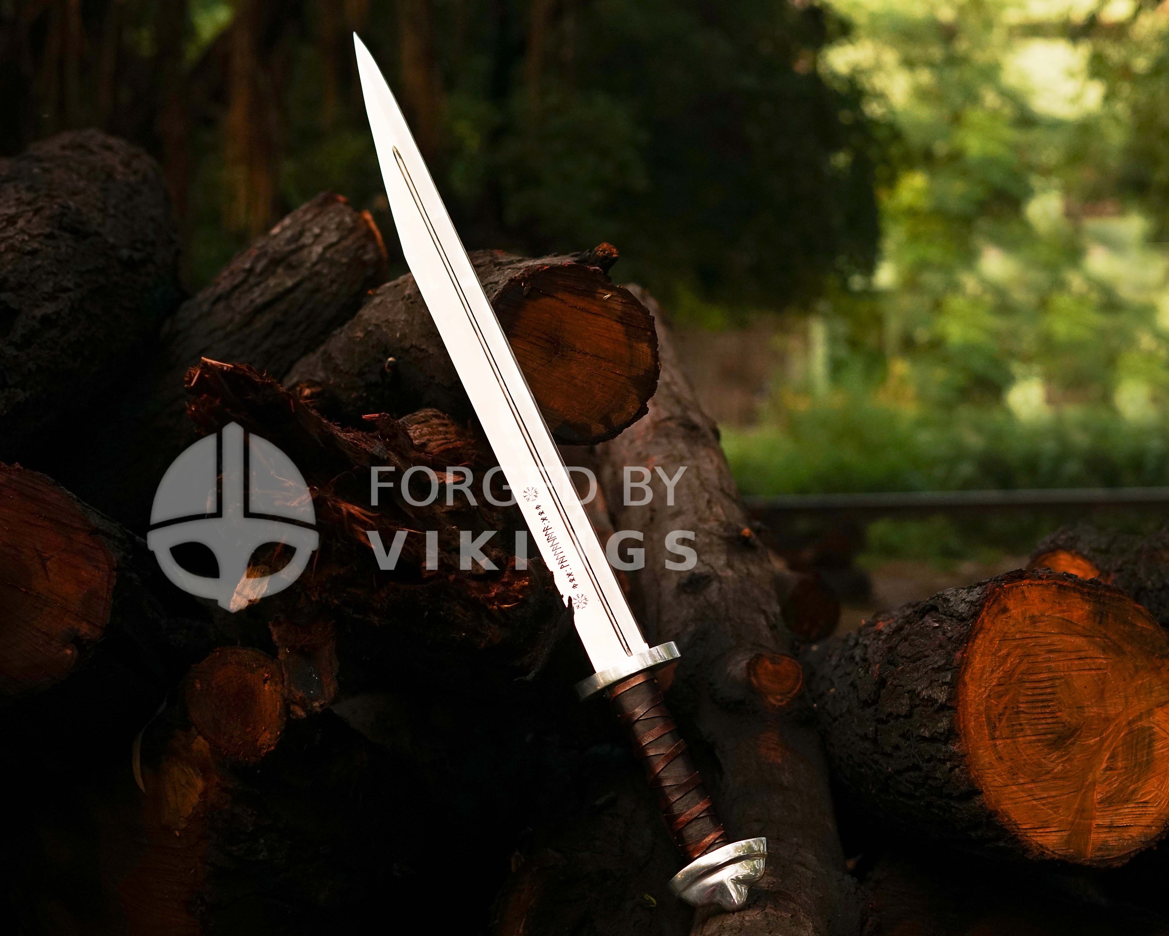 Hand-forged Viking Seax knife with detailed blade engravings resting on wooden logs.