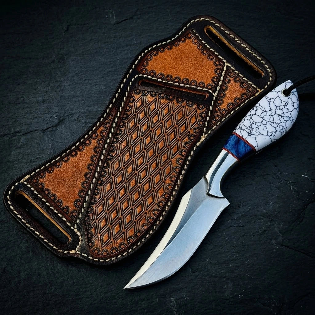 A custom fixed-blade hunting knife with a white cracked-pattern handle and blue bolster, placed flat next to an intricately stamped brown leather belt sheath on a dark textured background