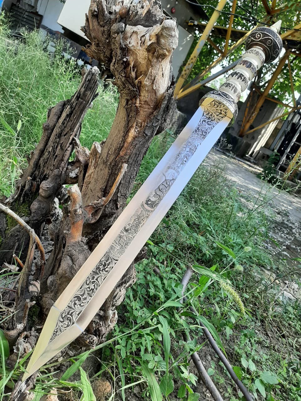 Full-length diagonal view of a handmade Roman Gladius short sword featuring an engraved blade and carved bone handle, resting on natural tree stump outdoors