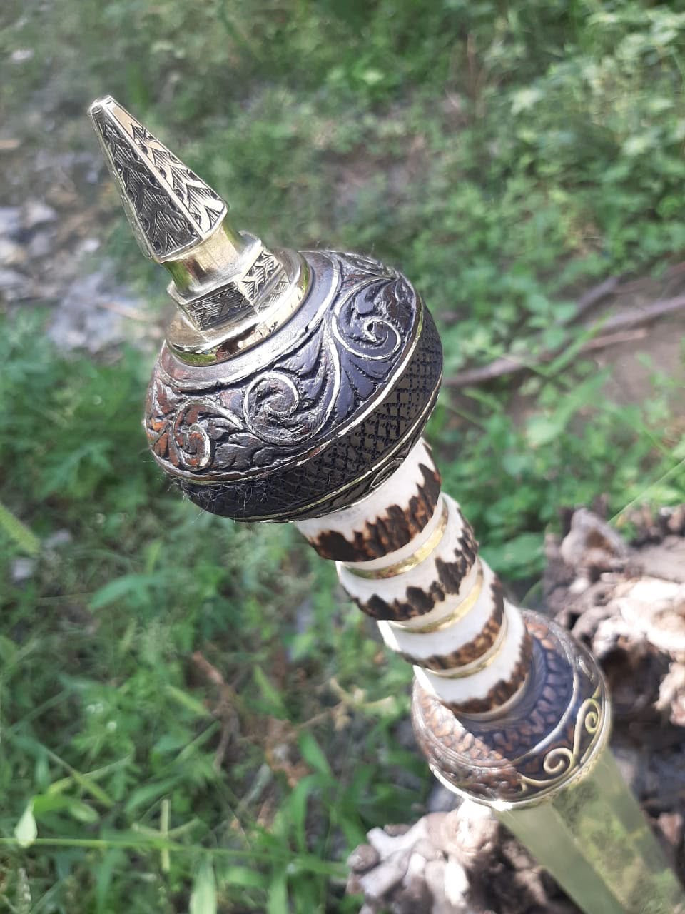 Close-up shot of a Roman Gladius short sword handle showing a carved bone hilt with brass spacers and an intricately engraved metal pommel.