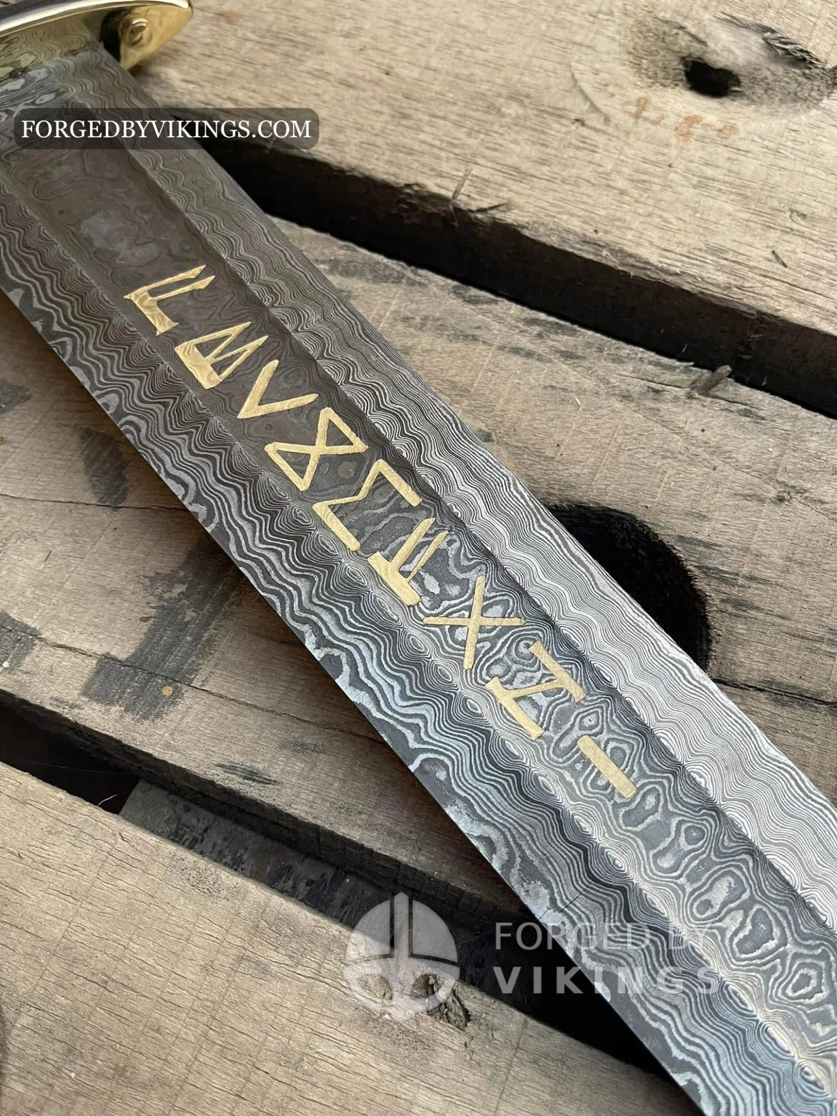 Extreme close-up shot of gold Elder Futhark runes inlaid on a pattern-welded Damascus steel Viking sword blade, resting on wooden planks