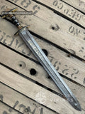 Handmade Viking sword with a pattern-welded Damascus steel blade inscribed with runes, featuring a ornate brass and dark wood hilt resting diagonally on a wooden crate surface