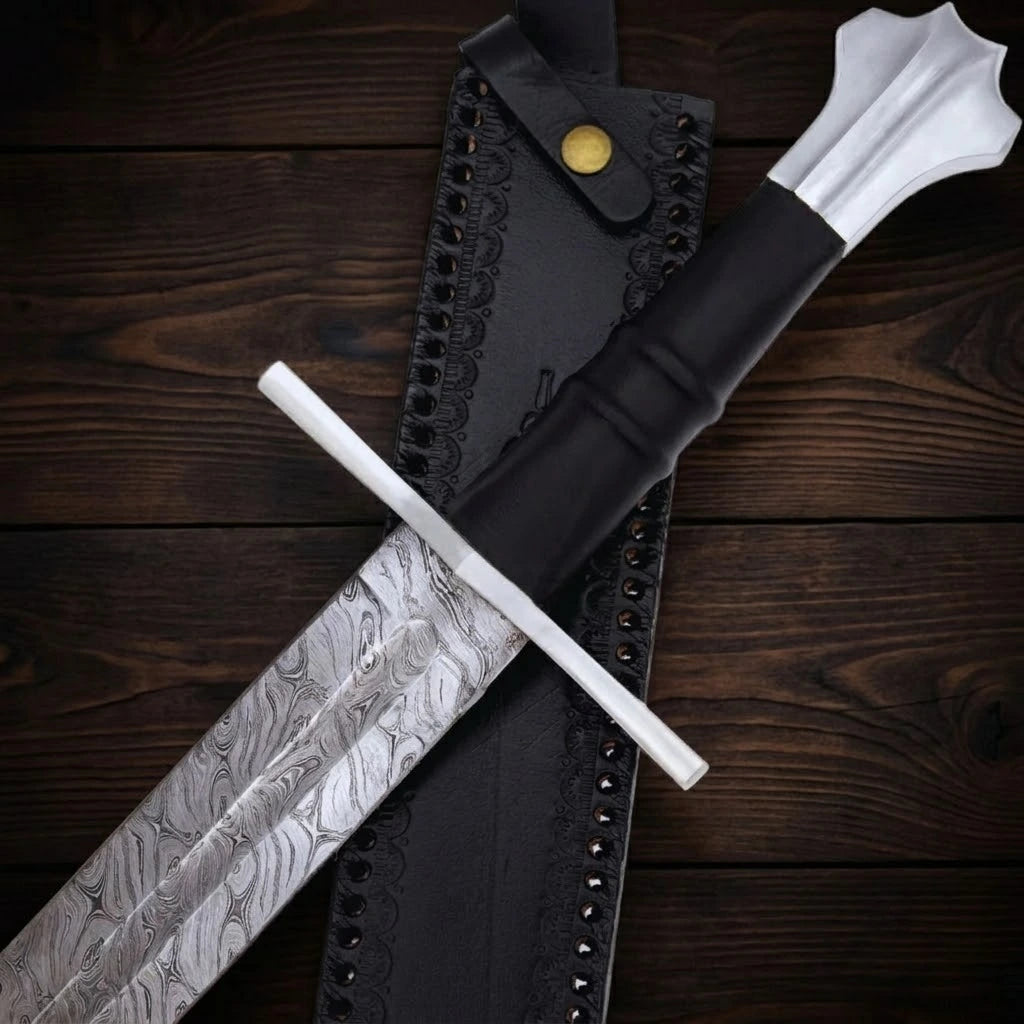 A detailed close-up shot of a custom medieval sword hilt, showcasing the flowing waves of the Damascus steel blade, a polished silver crossguard, a ribbed black handle, and a distinct fluted pommel resting on top of a black leather scabbard.