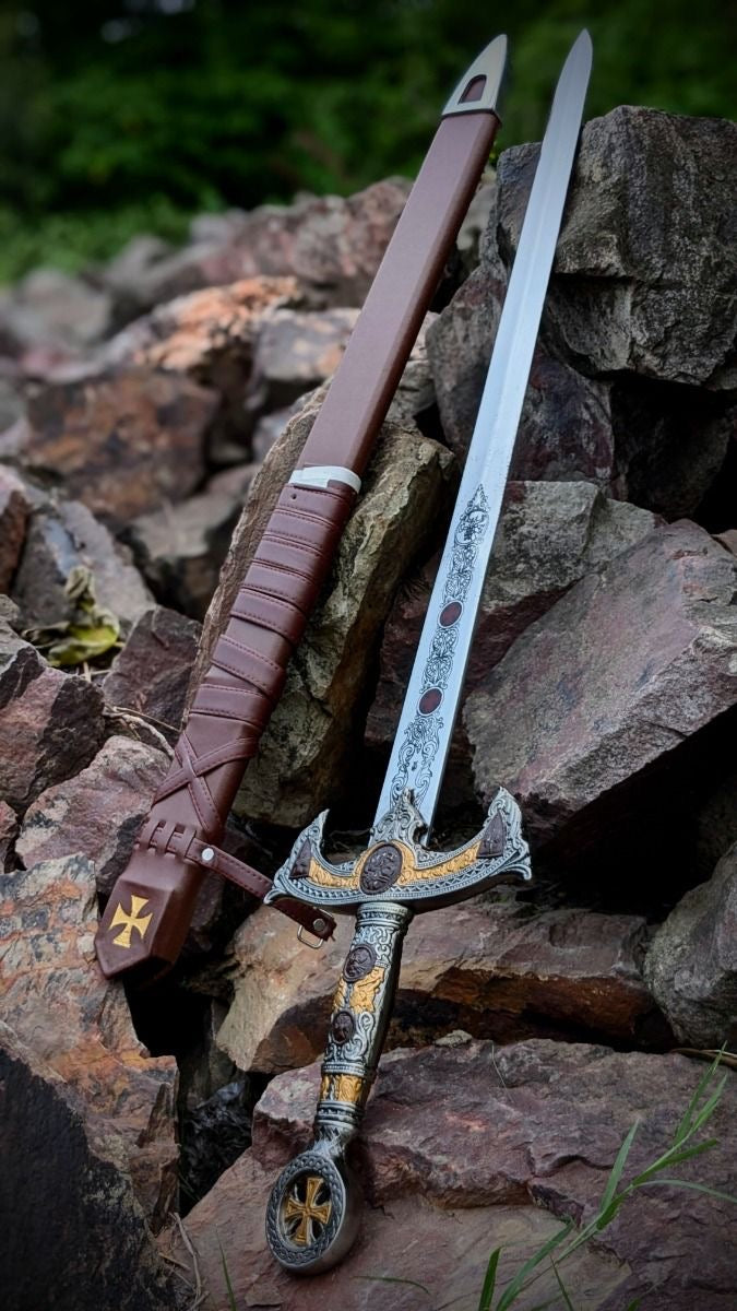 Close-up of an ornate Templar Knight sword and matching leather scabbard , featuring gold and silver detailing, intricate blade engravings, and resting on a textured rock background