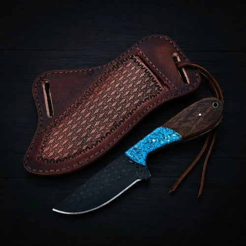 Handmade Buckaroo ranch knife crafted from dark forged rasp steel with a hybrid turquoise inlay and wood handle, shown with a textured brown leather pancake sheath on a dark wood background