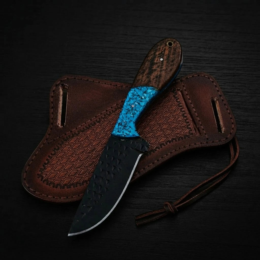 Top-down view of a handmade Buckaroo ranch knife with a dark forged rasp steel blade, turquoise inlay and wood handle, resting on a brown leather pancake sheath over dark wood.