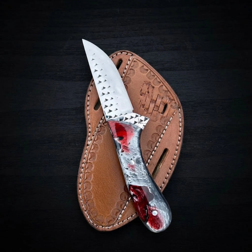 Handmade Rasp Steel Cowboy Knife with a red, black, and silver swirl resin handle lying on top of a tan stamped leather belt pouch sheath against a dark wooden background