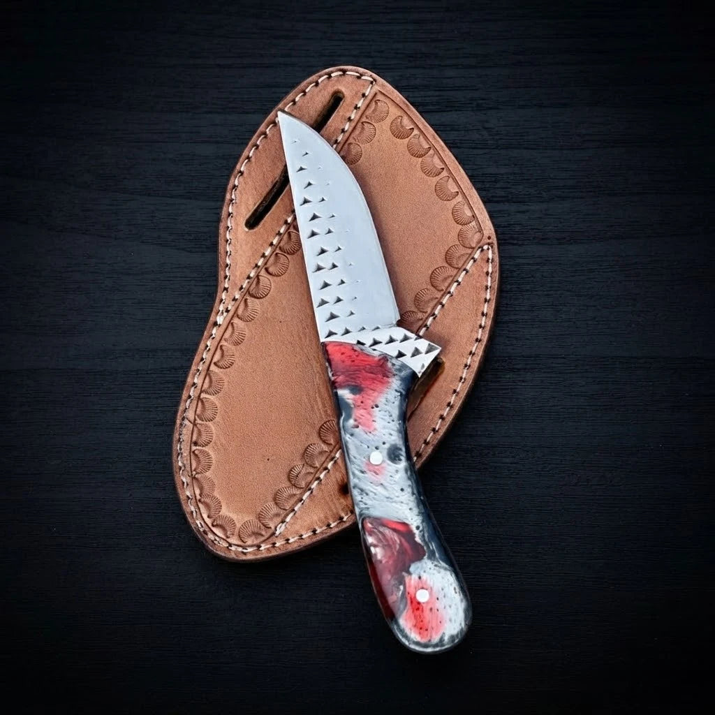 Handmade Rasp Steel Cowboy Knife featuring a red and silver resin handle resting on a tan stamped leather sheath against a dark background.