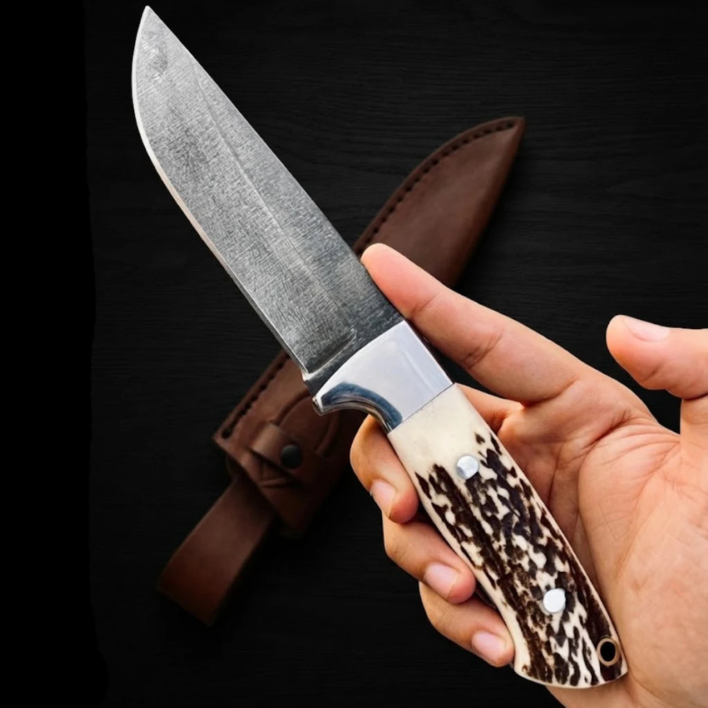 A hand gripping the Stag Ridge Hunter handmade hunting knife, showcasing the natural texture of the stag horn handle and steel bolster against a dark background.