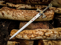 Close-up photo of a decorative Templar Knight medieval sword from image.png, featuring an intricate gold and steel handle, a cross-engraved blade, and resting on rustic stacked logs