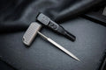 CNC machined titanium EDC push tool with a diamond-textured T-handle grip, displayed alongside its black sheath fitted with an UltiClip on a dark slate background