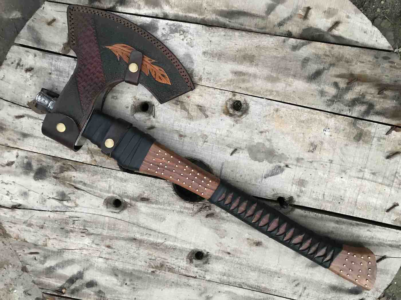 Custom Viking axe secured inside a detailed leather sheath with feather-inspired engraving, laid on a rustic wooden surface.